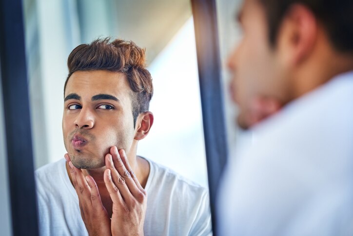 Shot of a handsome young man admiring looking at his face in the bathroom mirror