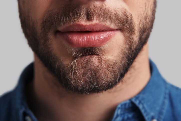 Close up of young unshaved man standing against grey background