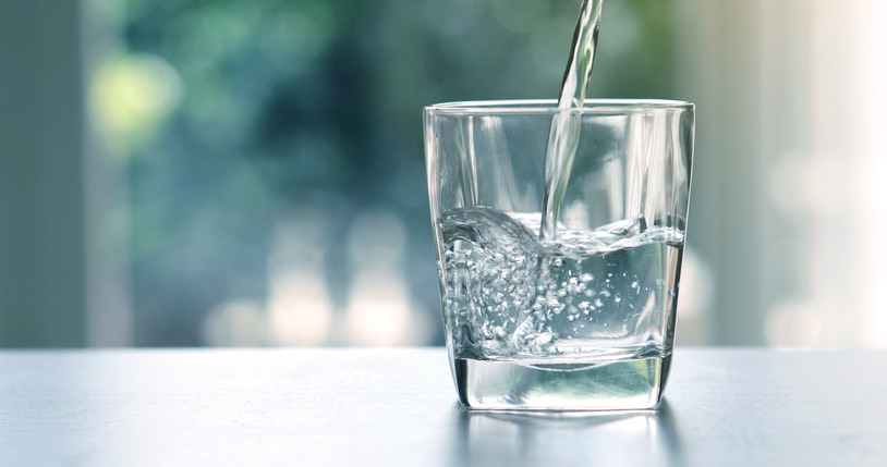 Close up pouring purified fresh drink water from the bottle on table in living room