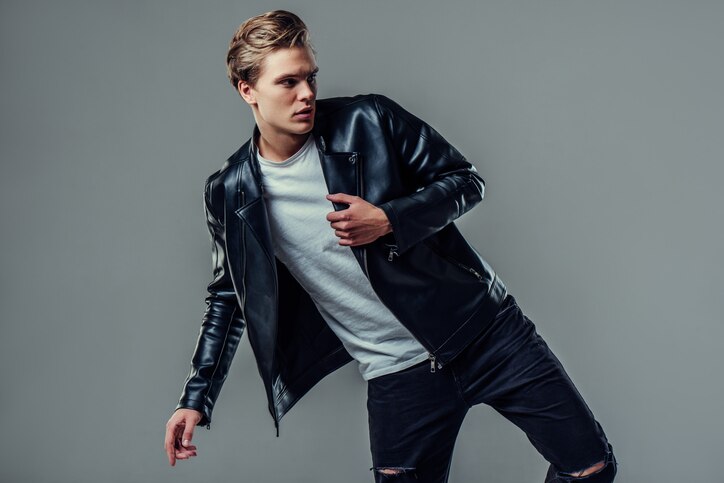 Handsome young man isolated. Fashionable  man in leather jacket is standing on grey background.